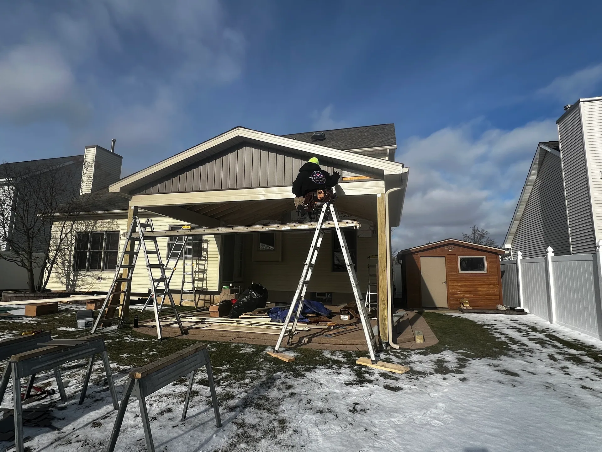 worker on ladder finishing covered patio gable soffit trim snowy yard shed silve