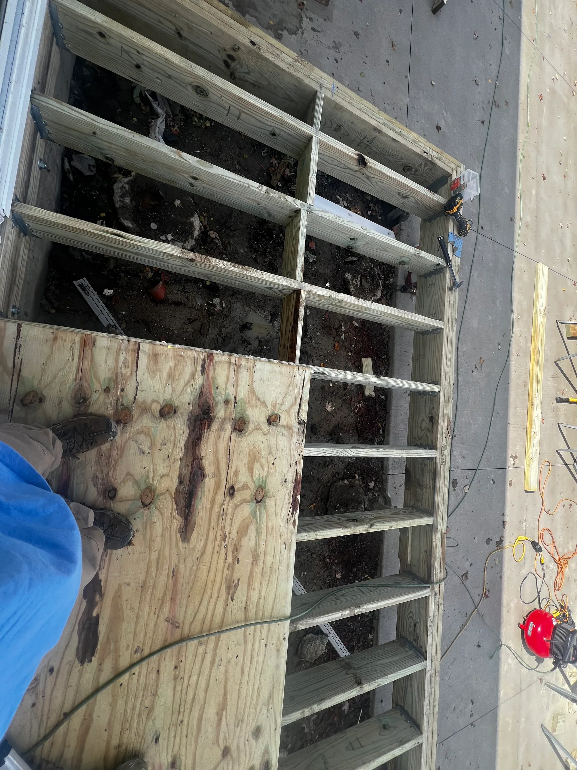 worker standing on plywood open floor joists dirt below porch frame silver sprin